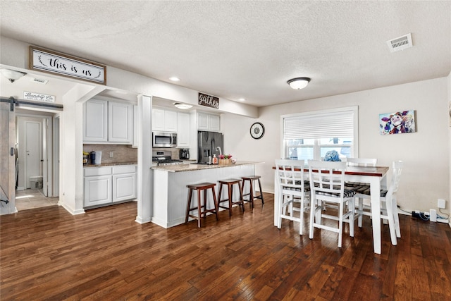 dining area with a textured ceiling, visible vents, a barn door, and dark wood-type flooring