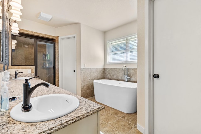 bathroom with tile walls, visible vents, a sink, a freestanding bath, and double vanity