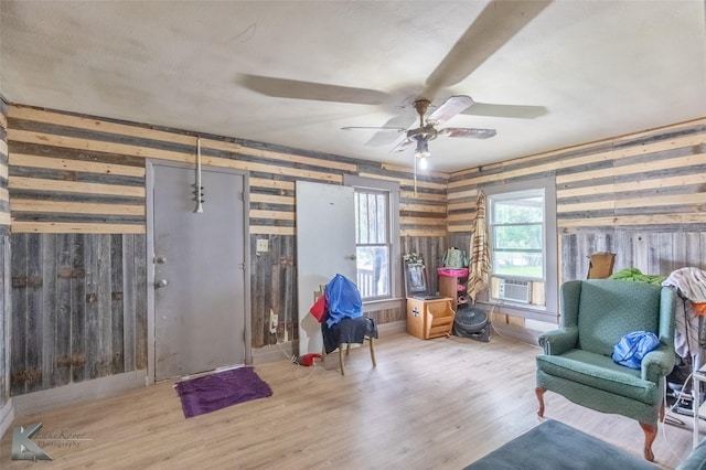 sitting room with ceiling fan, wood walls, cooling unit, and wood finished floors