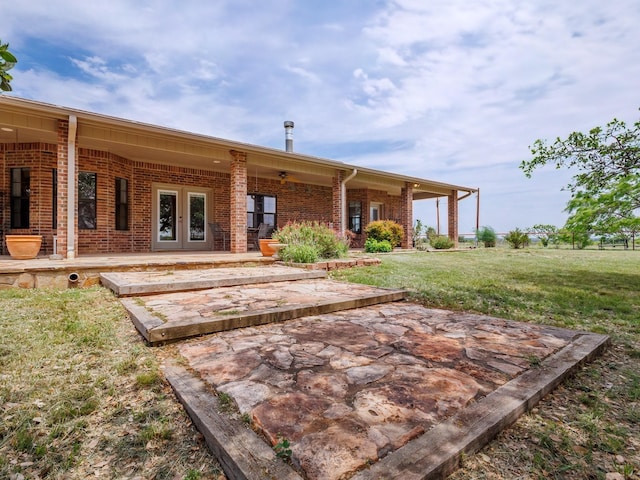 rear view of house with brick siding, a yard, a patio, and french doors