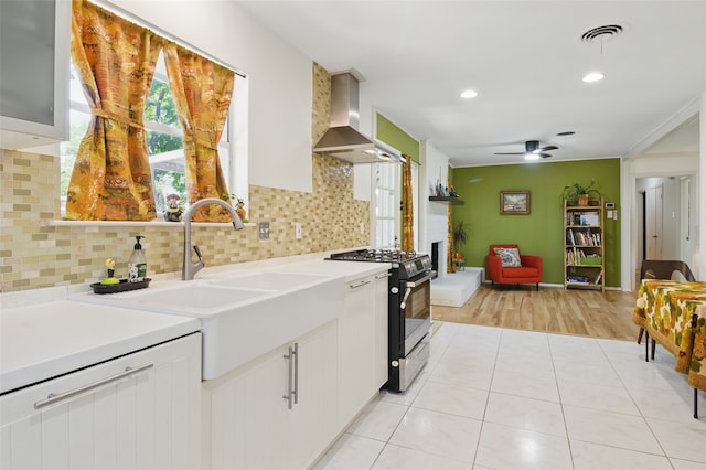 kitchen featuring wall chimney range hood, visible vents, light countertops, gas range, and a ceiling fan
