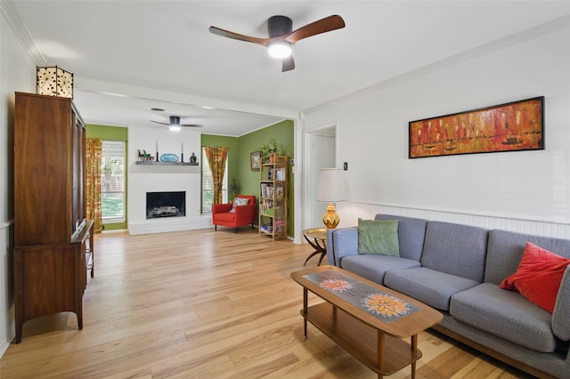 living room with a fireplace, crown molding, light wood-style flooring, and a ceiling fan