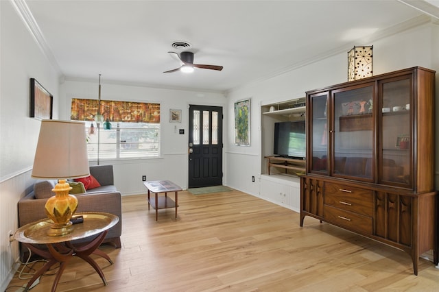 living area featuring ceiling fan, ornamental molding, a wainscoted wall, and light wood-style floors
