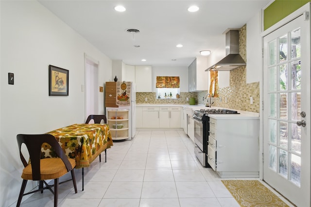 kitchen with wall chimney exhaust hood, backsplash, light countertops, white cabinets, and range with gas cooktop