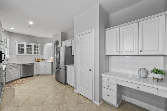 kitchen with stainless steel appliances, glass insert cabinets, white cabinets, light countertops, and tasteful backsplash