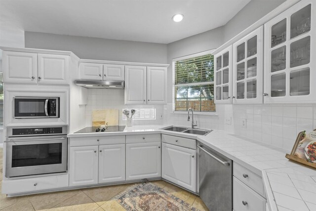kitchen with white cabinets, appliances with stainless steel finishes, glass insert cabinets, and a sink
