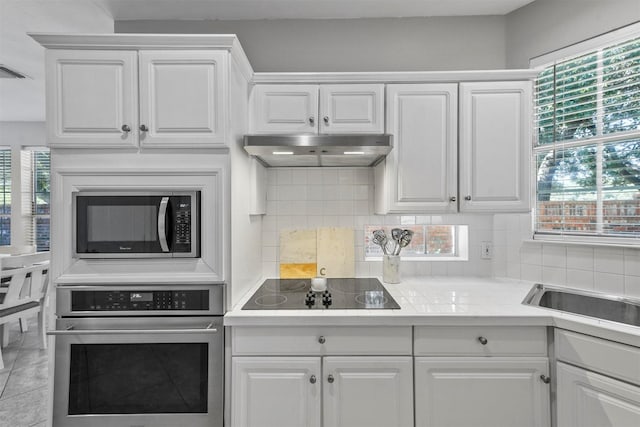 kitchen featuring stainless steel appliances, white cabinets, under cabinet range hood, and tasteful backsplash