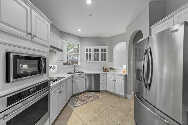 kitchen with a sink, under cabinet range hood, white cabinetry, decorative backsplash, and appliances with stainless steel finishes