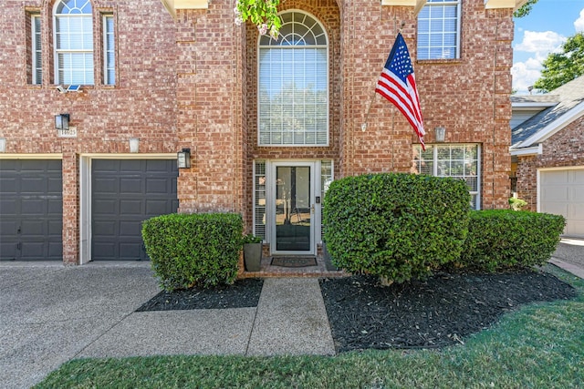 entrance to property featuring an attached garage, brick siding, and driveway