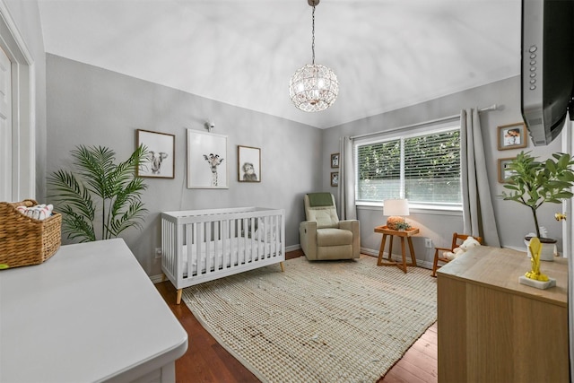 bedroom with wood finished floors, a chandelier, a nursery area, baseboards, and vaulted ceiling
