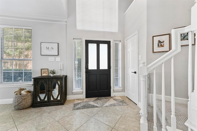 entryway featuring a high ceiling, crown molding, tile patterned flooring, baseboards, and stairs