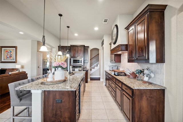 kitchen featuring a breakfast bar, visible vents, dark brown cabinetry, arched walkways, and stainless steel appliances
