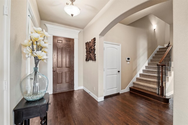 foyer entrance with arched walkways, stairs, baseboards, and dark wood finished floors