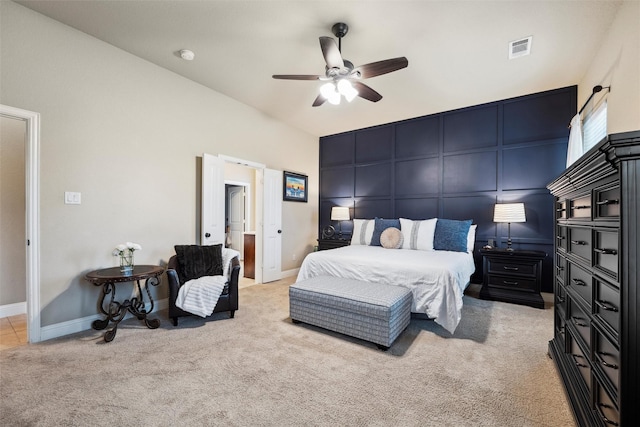 bedroom with a ceiling fan, visible vents, baseboards, a decorative wall, and light carpet