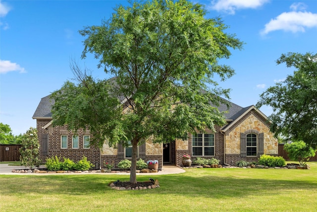 view of front of house featuring a front lawn, brick siding, roof with shingles, and stone siding