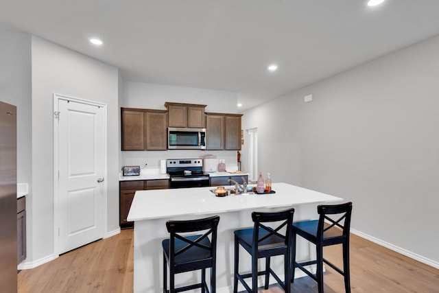 kitchen with light countertops, a breakfast bar area, stainless steel appliances, and light wood-style flooring