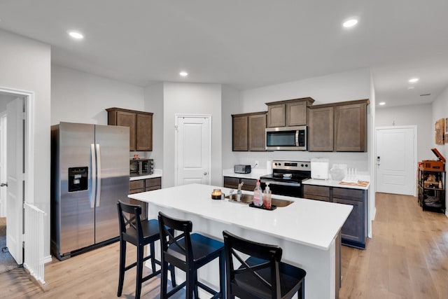 kitchen featuring a kitchen island with sink, dark brown cabinetry, light wood finished floors, light countertops, and appliances with stainless steel finishes
