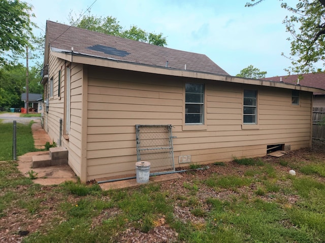 view of side of home with roof with shingles and fence