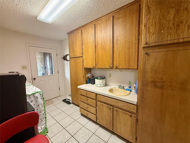 clothes washing area with a sink, a textured ceiling, and light tile patterned floors