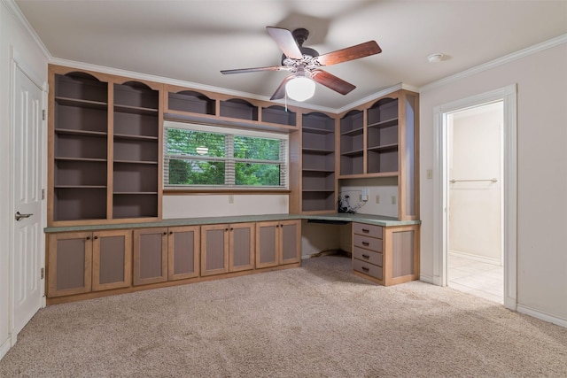 unfurnished office featuring built in desk, crown molding, light carpet, ceiling fan, and baseboards