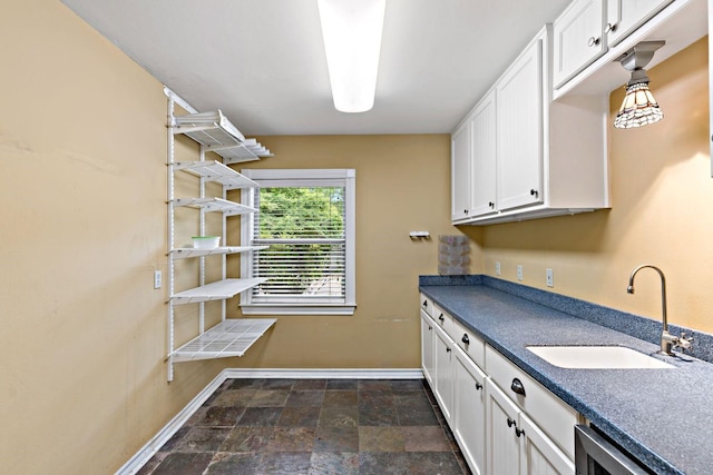 clothes washing area featuring baseboards, stone finish floor, and a sink