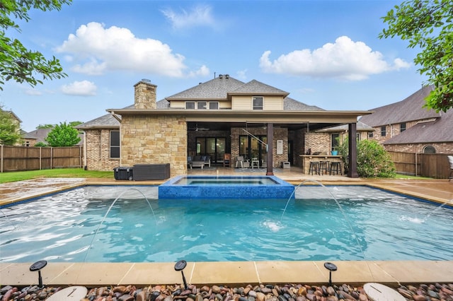 view of swimming pool featuring a pool with connected hot tub, fence, outdoor dry bar, an outdoor hangout area, and a patio area