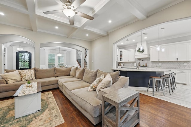 living room featuring beam ceiling, dark wood-style flooring, a ceiling fan, and arched walkways