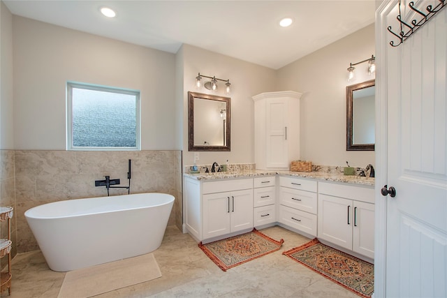 bathroom featuring double vanity, a sink, a soaking tub, tile walls, and recessed lighting