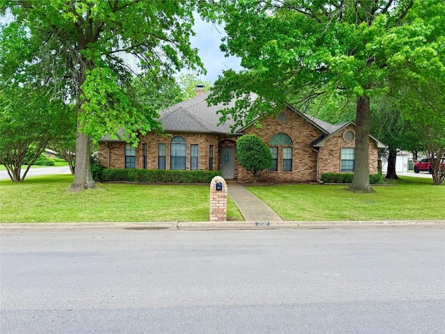 traditional home with a front yard, roof with shingles, and brick siding