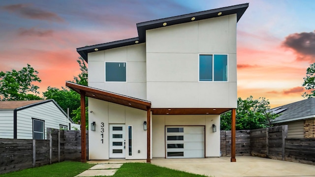 rear view of house with driveway, stucco siding, a garage, and fence
