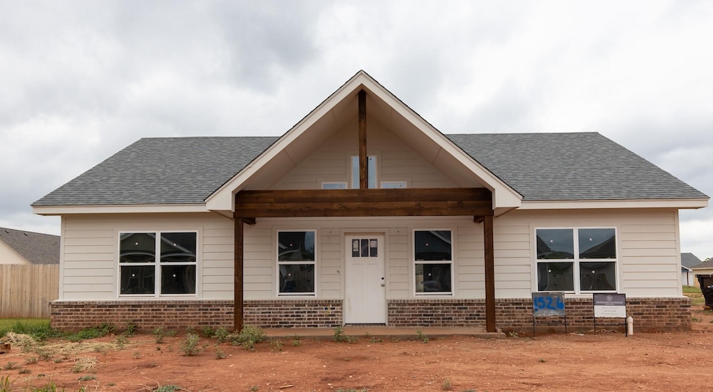 view of front of home featuring brick siding, roof with shingles, and fence