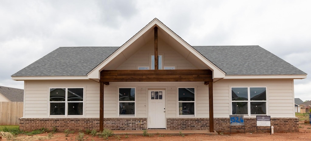 rear view of house featuring brick siding, a shingled roof, and fence