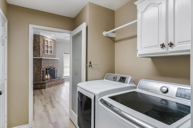 clothes washing area with cabinet space, independent washer and dryer, light wood finished floors, and a brick fireplace