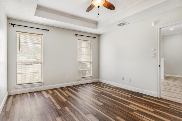empty room with a ceiling fan, visible vents, crown molding, wood finished floors, and a raised ceiling