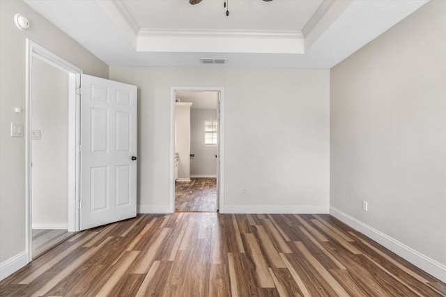 unfurnished bedroom with a tray ceiling, visible vents, and wood finished floors