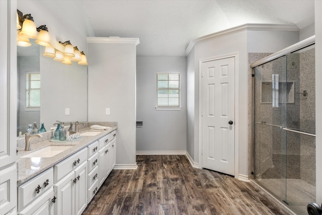 full bath with a stall shower, double vanity, a sink, and wood finished floors