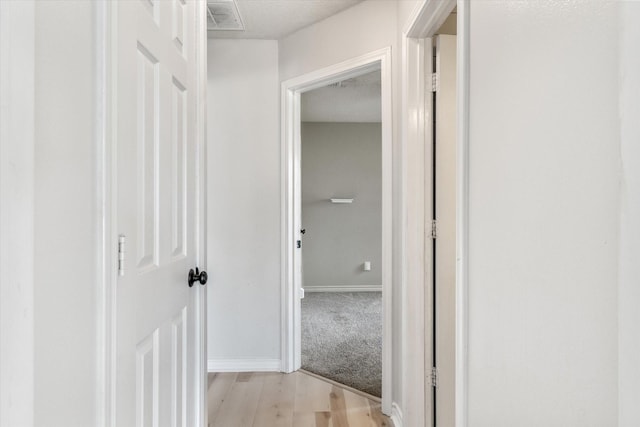 hall with baseboards, light wood-style flooring, and visible vents