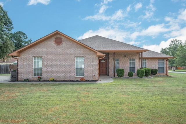 ranch-style home featuring a front lawn, a shingled roof, brick siding, and fence
