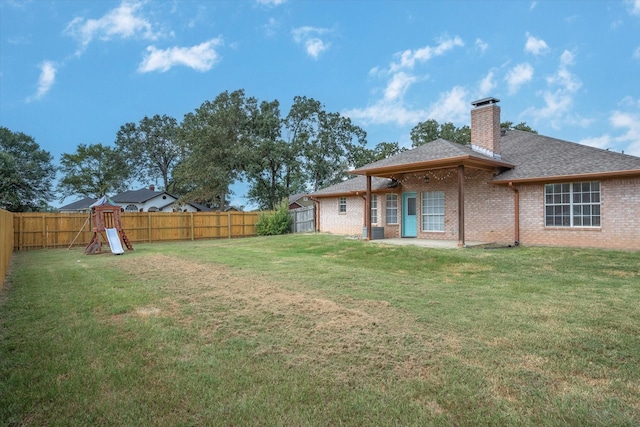 rear view of house featuring a fenced backyard, a chimney, a yard, and brick siding