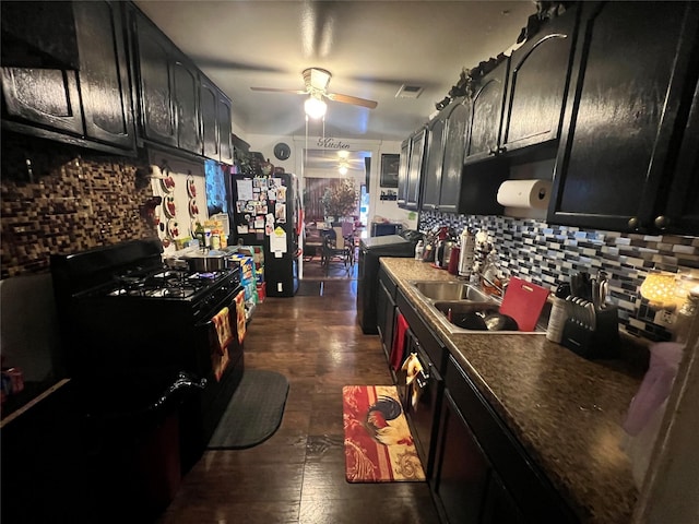 kitchen with black gas range oven, dark cabinets, a ceiling fan, visible vents, and decorative backsplash
