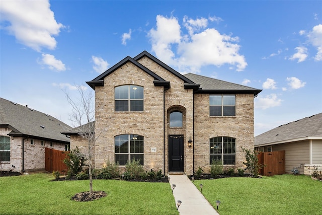 french country style house featuring brick siding, a front lawn, fence, and a gate