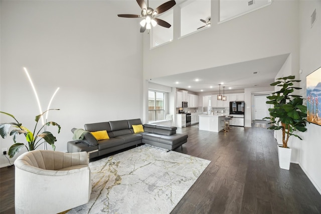 living room featuring a towering ceiling, visible vents, recessed lighting, dark wood finished floors, and ceiling fan