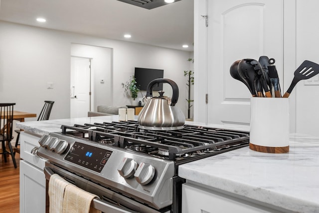 interior details featuring white cabinetry, gas range, light stone counters, and recessed lighting