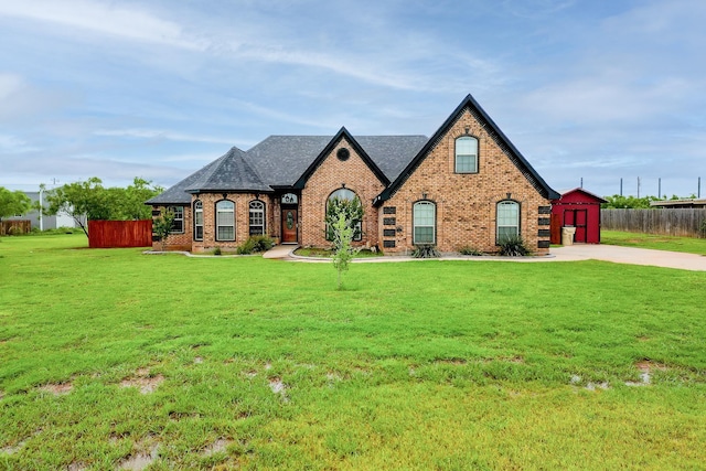 tudor house with a storage shed, fence, a front lawn, an outdoor structure, and brick siding