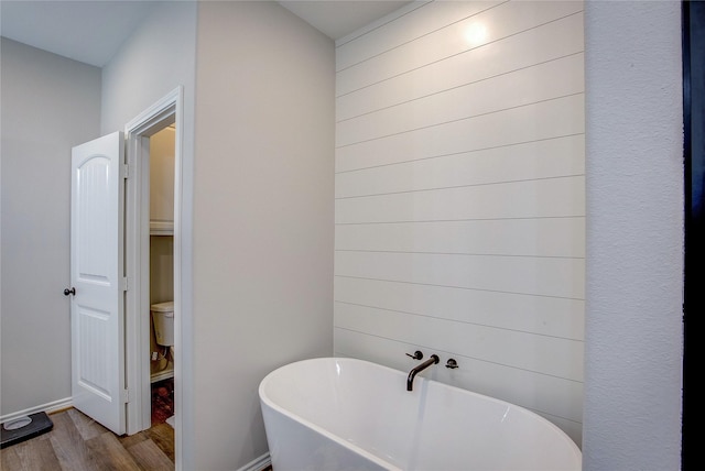 full bathroom with a soaking tub, toilet, baseboards, and wood finished floors