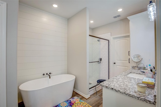 full bathroom with visible vents, a shower stall, vanity, a soaking tub, and wood finished floors