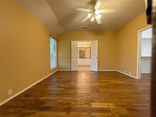 unfurnished bedroom featuring baseboards, ensuite bath, visible vents, vaulted ceiling, and dark wood-style floors
