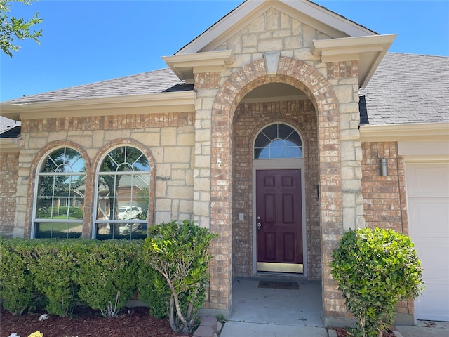 entrance to property featuring a shingled roof, brick siding, a garage, and stone siding