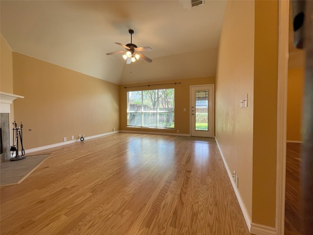 unfurnished living room with light wood-type flooring, vaulted ceiling, a ceiling fan, baseboards, and a tiled fireplace