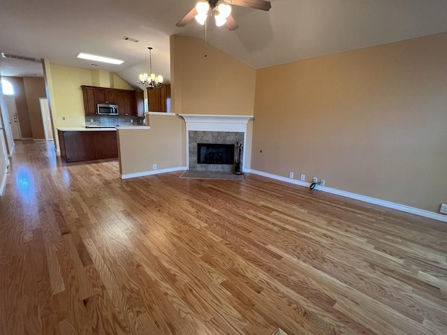 unfurnished living room with lofted ceiling, baseboards, ceiling fan with notable chandelier, light wood-style floors, and a fireplace
